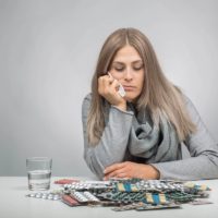Young woman is sitting in front of many pills Young woman is sitting in front of many pills, with one hand on her chin, looking down